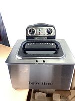 Front view of Bravetti Pro deep fryer showing stainless steel body, black handle lid, and control panel with knobs and indicator lights