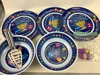 Five Chanukah-themed ceramic plates and bowls with menorah and dreidel designs, two metal latke servers, and six small plastic dreidels.