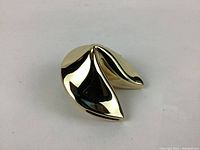 Metal decorative fortune cookie with shiny gold finish shown on white background.