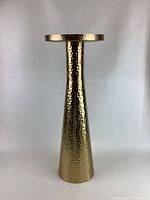 Tall gold stand with tapered cylindrical shape and hammered metal finish as a decorative accent piece.
