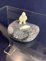 Front angle view of miniature indigenous Inuit stone sculpture showing the hunter figure and seal on a dark stone base.
