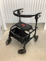 Front three-quarter angle showing the black folding walker with padded seat, storage bag, foam handle grips, and front wheels.