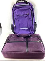 Front view of both purple luggage pieces showing the backpack upright and laptop bag in front