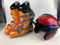 Photo showing orange Salomon ski boots and red Salomon racing helmet together on white background.