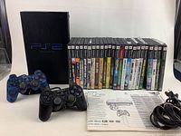 Sony PlayStation 2 console with two controllers, 20 video games lined up, and an instruction manual.