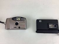 Two vintage 35mm cameras displayed side by side on a white surface. Left: Fujifilm Clear Shot. Right: Kodak Disc 3100.
