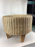 Side view of round wicker foot stool showing woven wicker sides and tapered wooden legs.