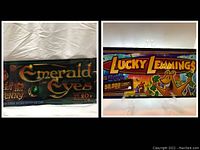 Two side-by-side images showing each large slot machine belly glass: Emerald Eyes on the left and Lucky Lemmings on the right, with vibrant, detailed artwork.