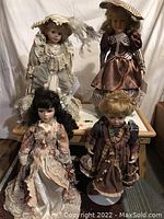 Photo of 4 porcelain dolls seated and standing on a table, showing full outfits and facial details
