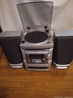 Full view of AIWA CX-ZL100 stereo system showing turntable with transparent dust cover atop the main unit, dual cassette players below, and two large speakers flanking the system.