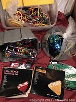 Photo showing 4 K'NEX kits combined with bags and bins of parts, instruction manuals, and a robotic head model made from K'NEX.