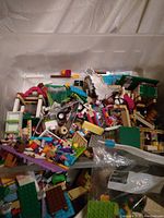 Top-down photo of a plastic tub filled with assorted Lego pieces and small assembled structures in multiple colors.