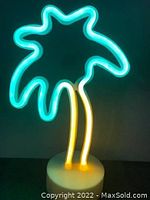 Palm tree shaped neon lamp illuminated showing blue-green neon leaves and yellow neon trunk on a white base.