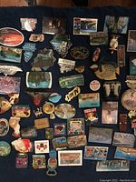 Overview photo showing a collection of over 60 assorted souvenir magnets arranged closely on a dark surface. The magnets depict various global landmarks, cultural symbols, animals, and scenic imagery.