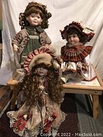 Three porcelain dolls posed on a small wooden table, showing detailed clothing and faces