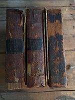 Top view of three antiquarian leather bound books showing heavily worn, cracked, and peeling dark brown leather spines with black labels and faded gold lettering.