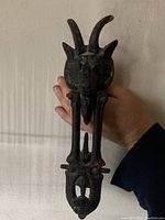 Front view of antique Victorian goat head door knocker held by hand showing full length and detailed goat face with curved horns.