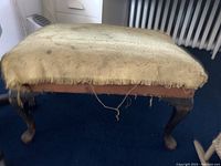 Photo of worn wooden footstool showing heavily damaged, frayed fabric upholstery needing replacement