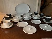 Full set of mid-century modern Rosenthal china showing white and black cups, saucers, plates, and covered dishes arranged on table.