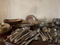 Overview of vintage silver plate serving pieces and cutlery arranged on a table, showing the variety of bowls, trays, and utensils included.