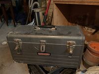 Closed vintage gray Craftsman metal toolbox with two latch clasps and a handle on top, showing wear and rust spots.
