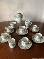 Full view of Wedgwood Santa Clara coffee pot, creamer, sugar bowl, 4 demitasse coffee cups with saucers, one tea cup with saucer, and an extra demitasse coffee cup without saucer on a wooden table.