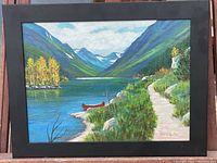 Frontal view of the oil painting showing the detailed lakeside landscape with a red canoe, path, trees, and mountains, framed in black.