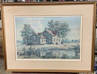 Framed vintage artwork showing stone house with surrounding trees and pond reflecting the scene, signed by Kierstied.