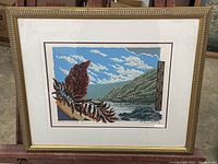 Framed vintage nature artwork showing landscape with leaves in foreground and signature, with gold decorative frame