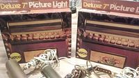 Two Satco Deluxe 7-inch picture lights with boxes behind, showcasing product packaging and condition.