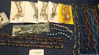 A broad view of most jewelry pieces including multiple necklaces, earrings attached to cards, and bracelets spread on a blue surface.
