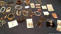 Full view of assorted bracelets and earrings on a dark surface with lot tag visible