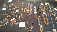 Wide shot of various costume jewelry necklaces laid out on a flat surface, showing different styles and materials including beads, chains, and pendants.