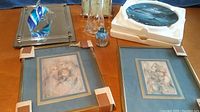 Photo showing two framed art prints, a glass dolphin figurine, a clear glass bottle, and a gold-framed clock and chrome-framed mirror in the background.