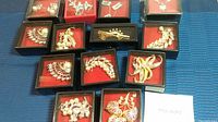 Photo overview of all 13 jewelry pieces arranged in black boxes with red velvet lining on a blue fabric background.
