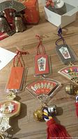 Five sets of Feng Shui wind chimes on a wooden surface including plaques with Chinese characters, fans with gold figures, multicolored cords, metal bells, and red tassels.