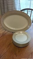 Full view of large oval platter and stacked dessert plates showing ivory base and gold lattice patterned rims.