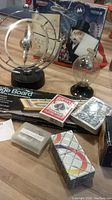 Photo showing a variety of games and gadgets including the cribbage board, playing cards, metallic spinning gadget, and a novelty glass globe on a stand.