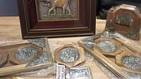Two teak coaster sets with metal engraved inlays, a small metallic bookmark, and a framed Thai elephant metal art piece on a wooden table.