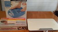 Homemedic Reflexology Foot Massager with Heat in box, two Battle Creek Thermophore Moist Heat Packs, and white serving tray on wooden table.
