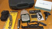 Photo of various pocket tools, knives, compact radio light, glass cutter, and small socket tool laid out on a table