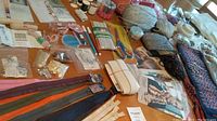 Photo of sewing, needlepoint, and crafting supplies arranged on a table, showing zippers, buttons, yarn balls, elastic bands, and crafting tools.