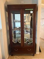Front view of Stanley Furniture wooden cabinet with glass doors and interior glass shelves, items displayed inside.