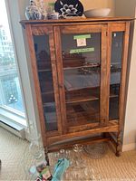 Full front view of wood display cabinet showing glass front, interior shelves, turned legs and decorative top molding