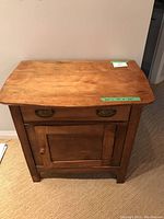 Front view of small wooden cabinet showing drawer and door closed with visible dimension labels on top.