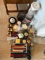 Wide shot showing collection of candles and holders including boxed taper candles, pillar candles, votives, candle holder baskets, and ceramic holders.