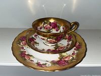 Close-up of one tea cup set with saucer and side plate showing rose pattern and gold trim