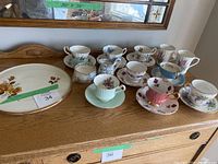 Photo of the full set on wooden sideboard including cups, saucers, creamer, sugar bowl, mugs, and serving dish
