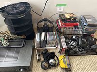 Overview of stereo receiver, Ideamade CD tower, multiple CDs and DVDs, headphones, Sony Walkman, chargers, and other electronics on carpet.