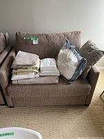 Front view of brown fabric hide-a-bed sofa with folded bedding and duvet bag on seat